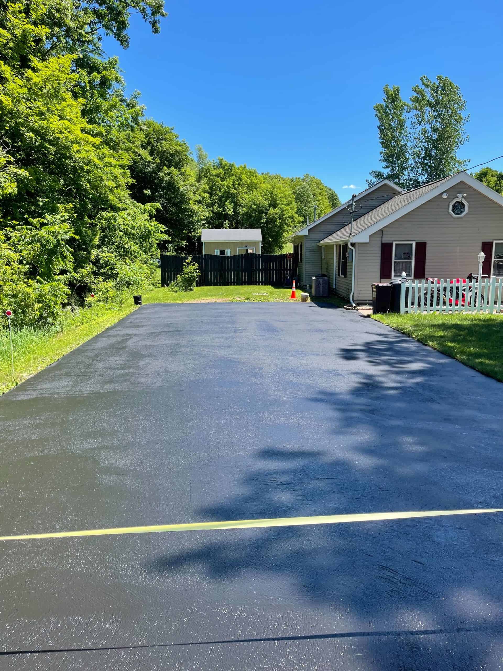 a rectangular asphalt driveway with sealcoating applied to the surface for drying in the sun