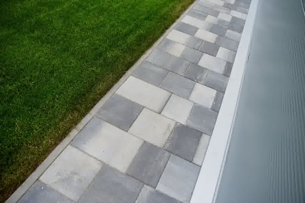 Modern gray concrete paver walkway runs alongside a lush green lawn, providing clean edging and contemporary curb appeal.