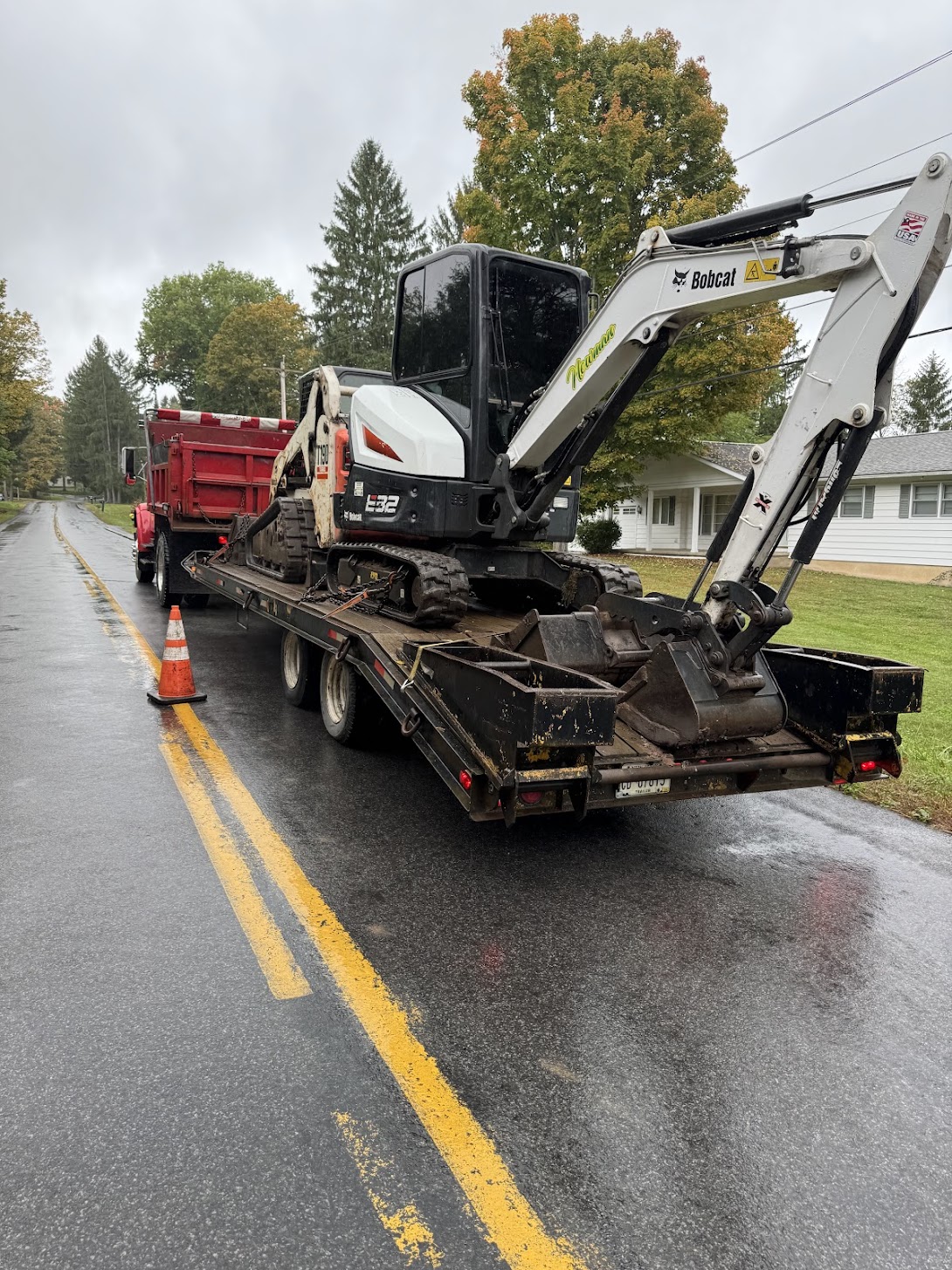 Bobcat E32 excavator and T190 skid steer secured on flatbed trailer, staged for transport to an excavation job site.