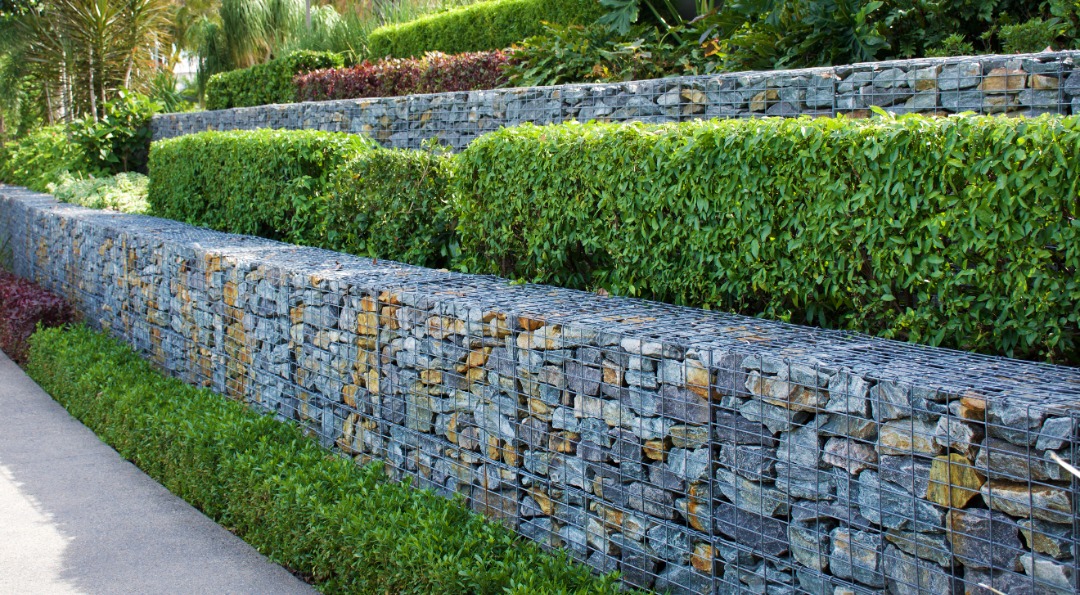 Tiered gabion retaining walls filled with stacked stones, integrated with greenery and shrubs for a modern landscape design.