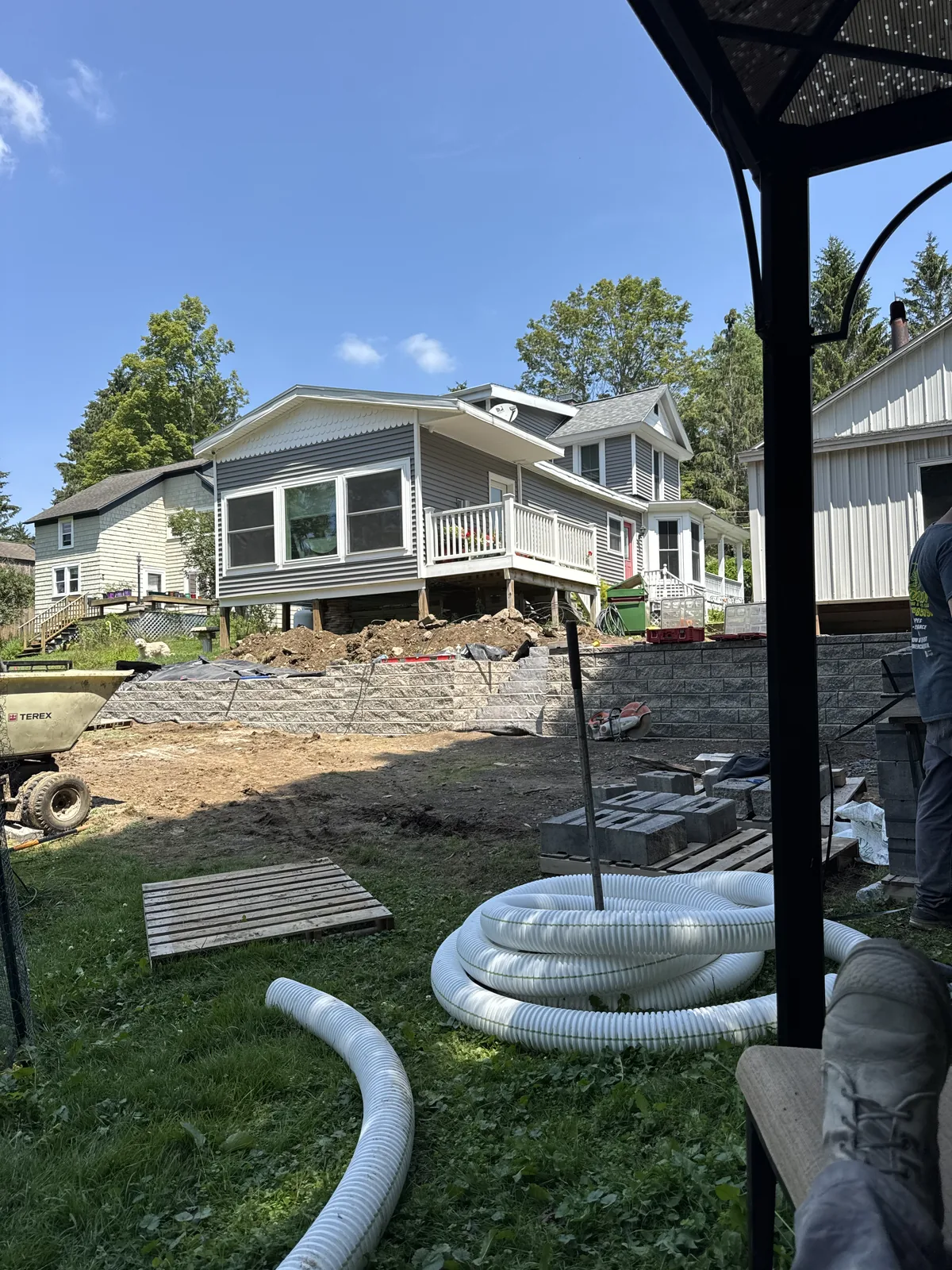  Drainage installation underway at a residential property with exposed foundation, retaining wall, and drainage pipes on site.


