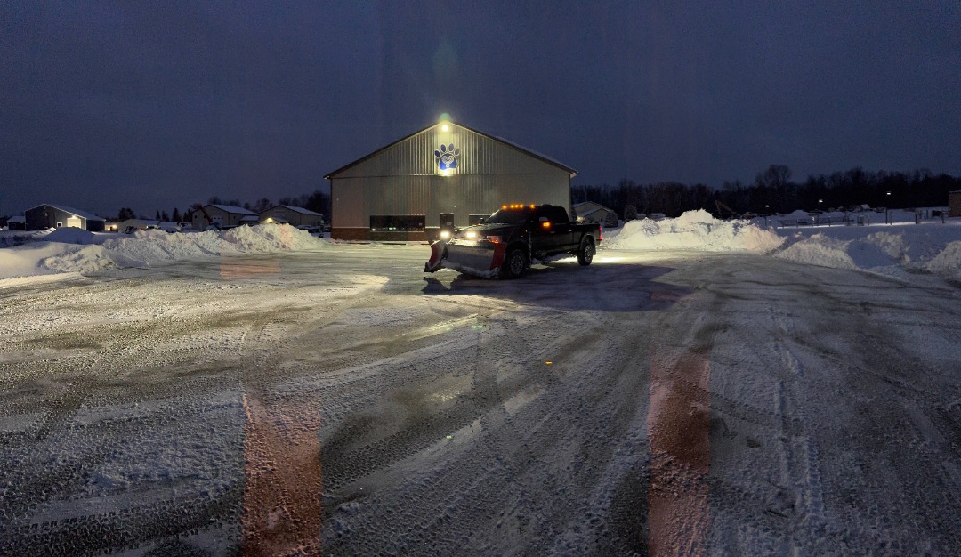 Snow removal truck clearing a commercial parking lot at night, pushing snow into piles for safer customer access.