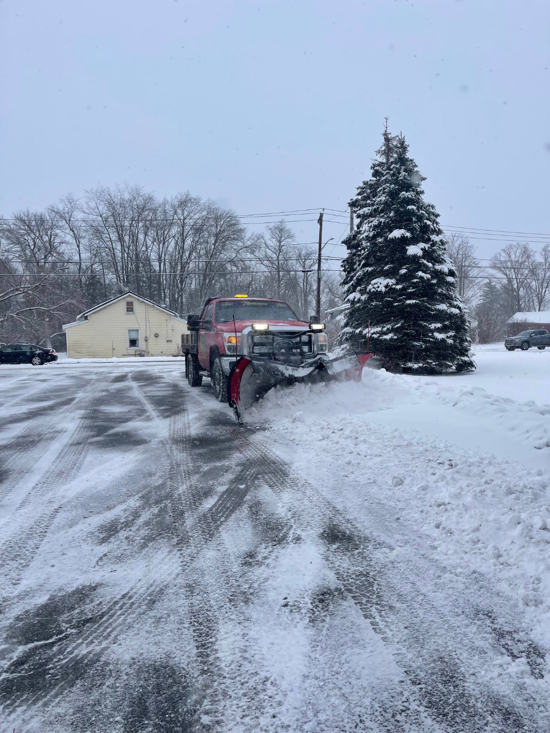 Red plow truck performing snow removal along a residential driveway with cleared tire paths and safe winter access.