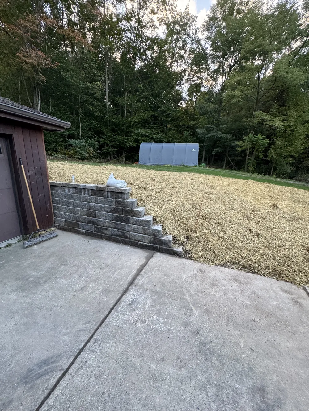 Straw covered yard and retaining wall showing drainage preparation to protect patios and walkways during Utica winters.