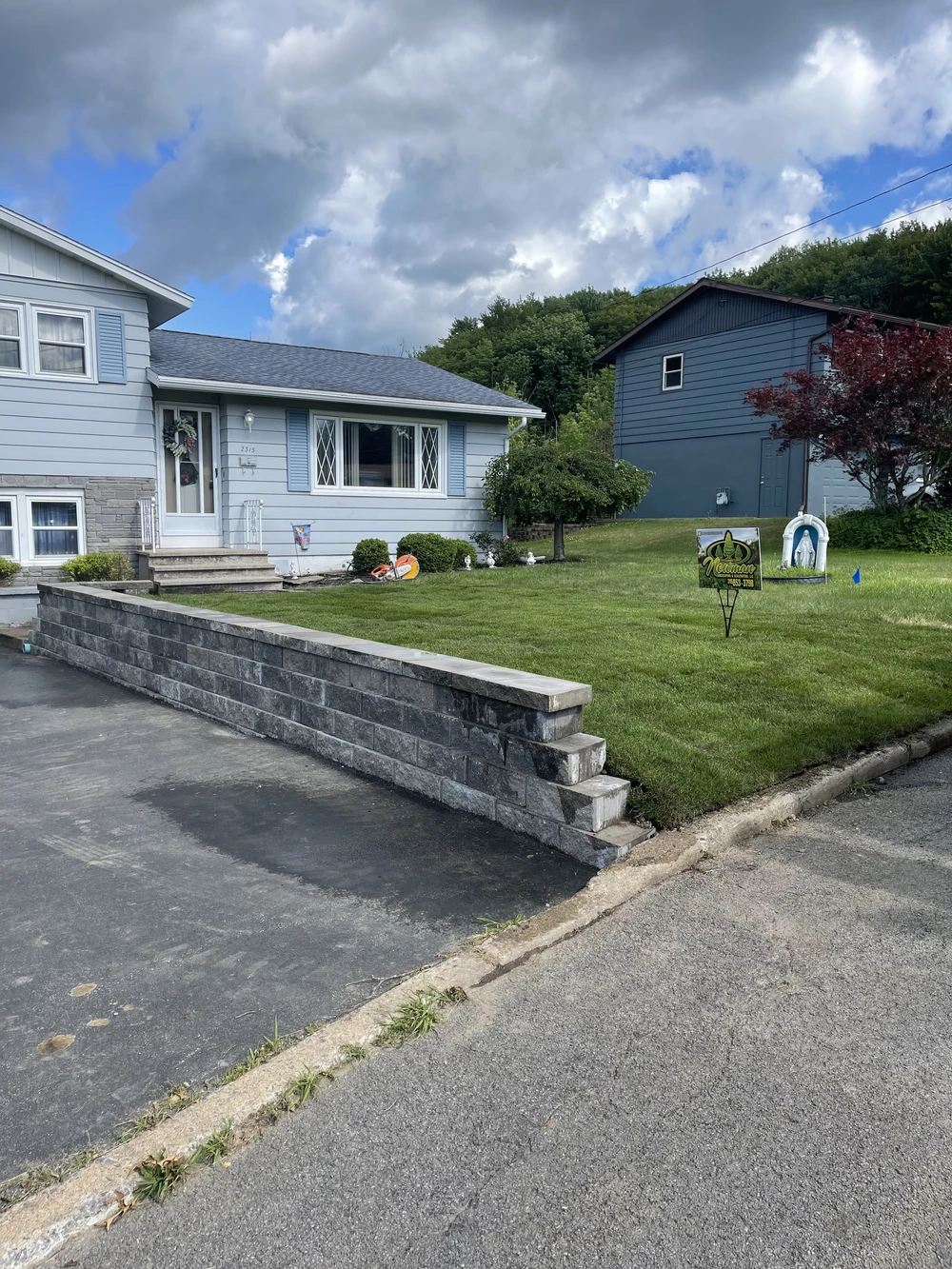 Front yard retaining wall bordering a driveway with steps leading to a home and healthy lawn.