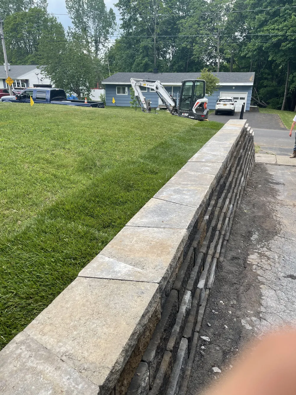 Tall retaining wall with capstones edging a driveway and graded lawn during landscape construction.