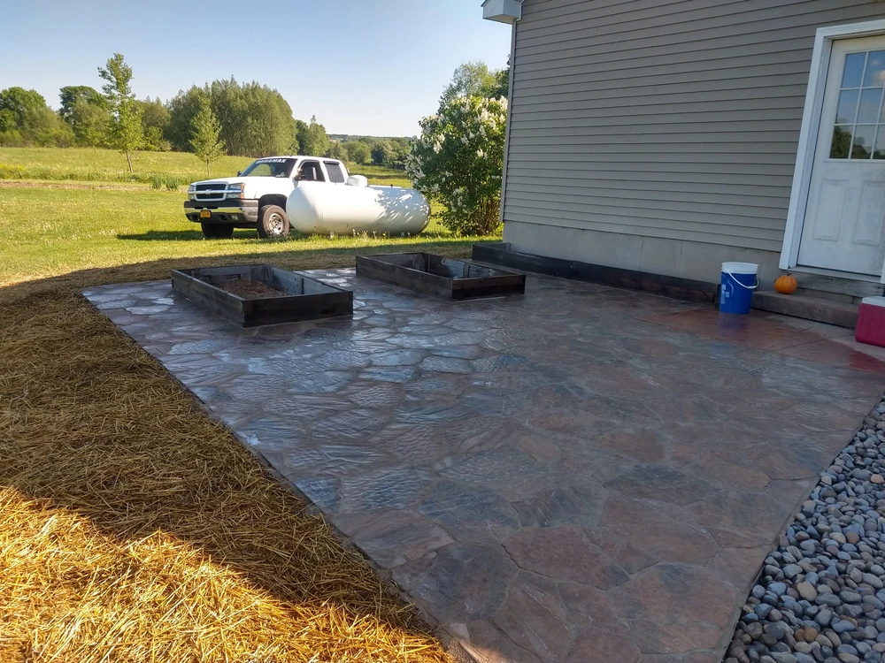 Newman Landscaping outdoor living spaces westmoreland ny 1 - Newman Landscaping & Excavating Stamped hardscaping patio beside the home includes raised planters and a wide space for outdoor seating.