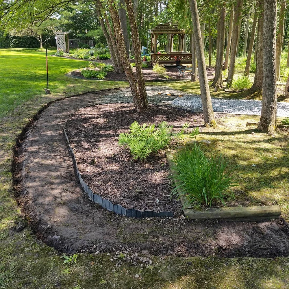 Spring landscaping redefines curved garden beds with fresh mulch edging around trees in a shaded backyard.